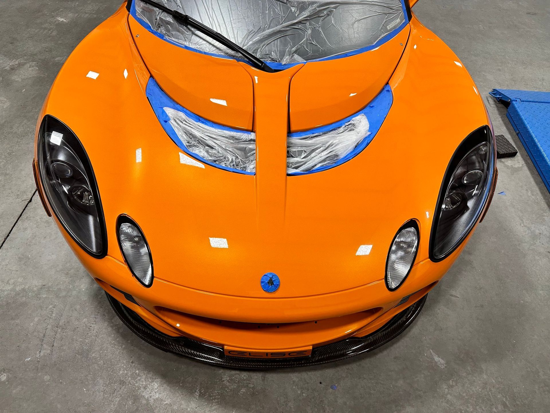 The front of an orange sports car with blue tape on it