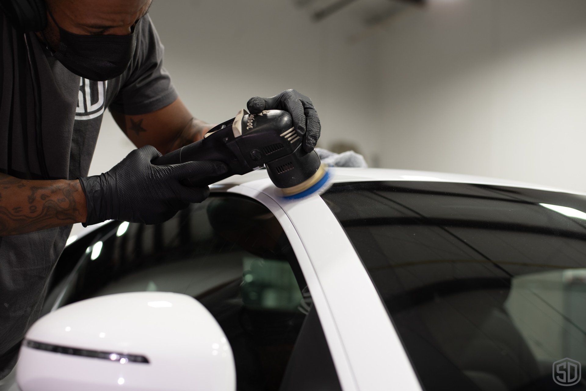 A man is polishing a white car with a machine.
