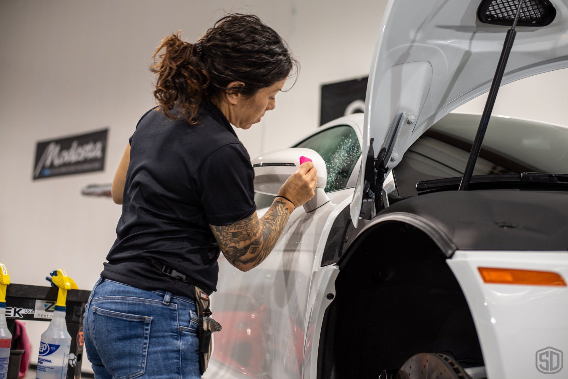 A woman is cleaning a white car in a garage.