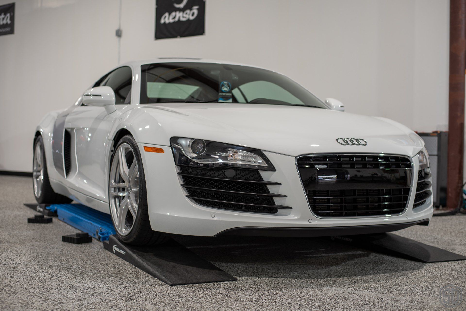 A white audi r8 is parked on a ramp in a garage.