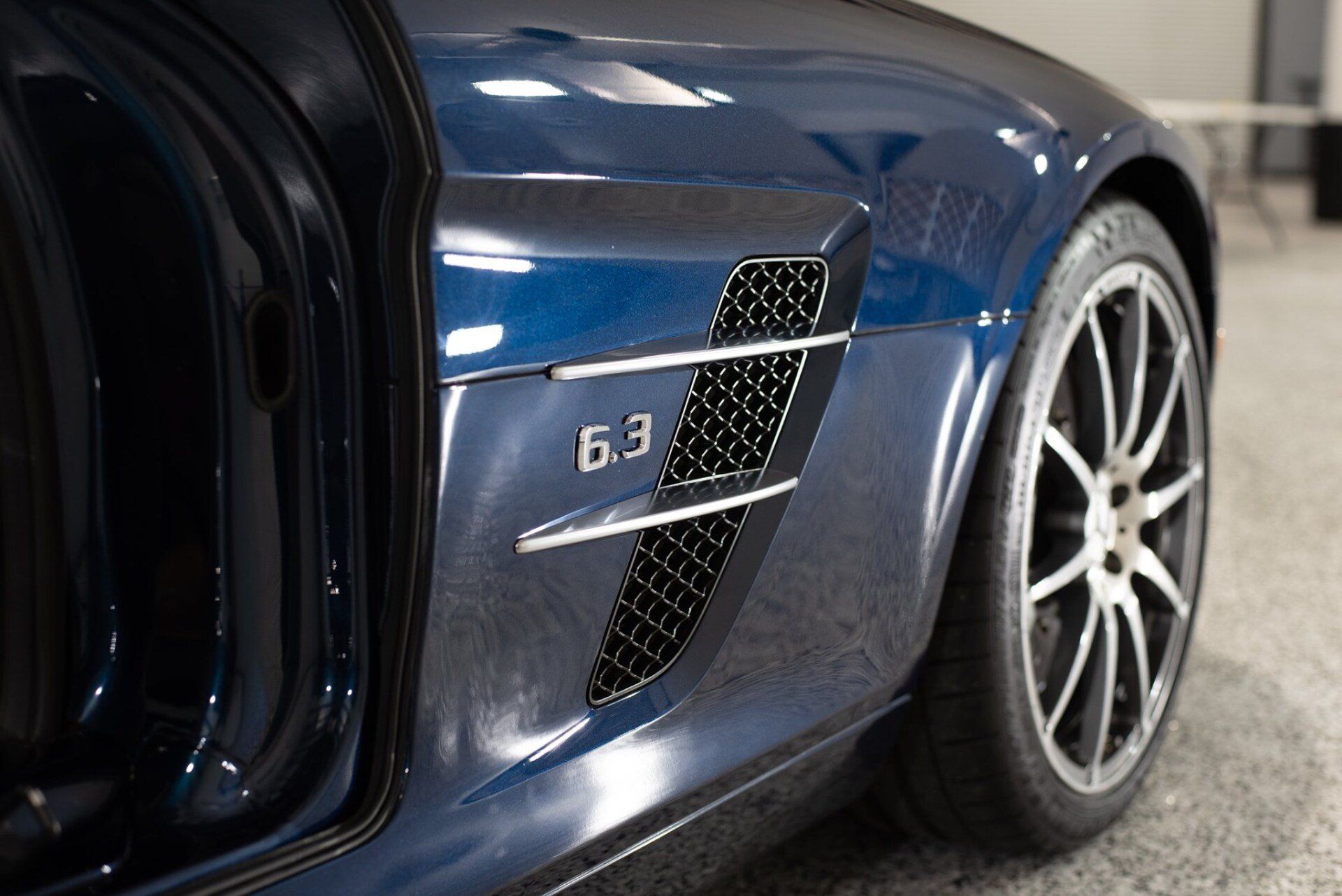 A blue sports car with the door open is parked in a garage.