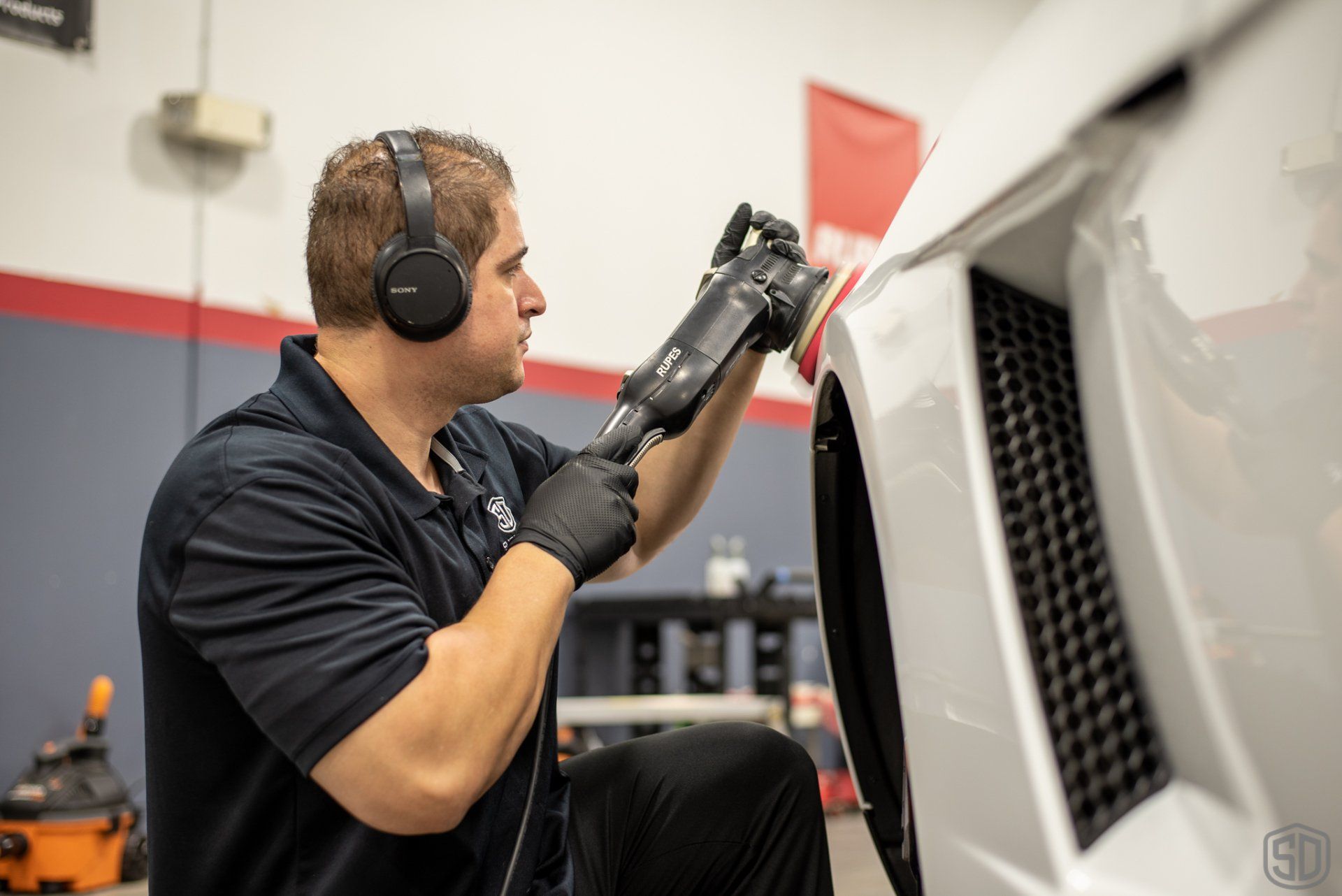 A man wearing headphones is polishing a car in a garage.