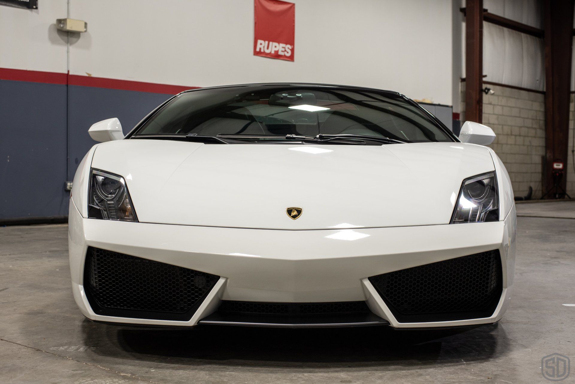 A white lamborghini is parked in front of a rupes sign