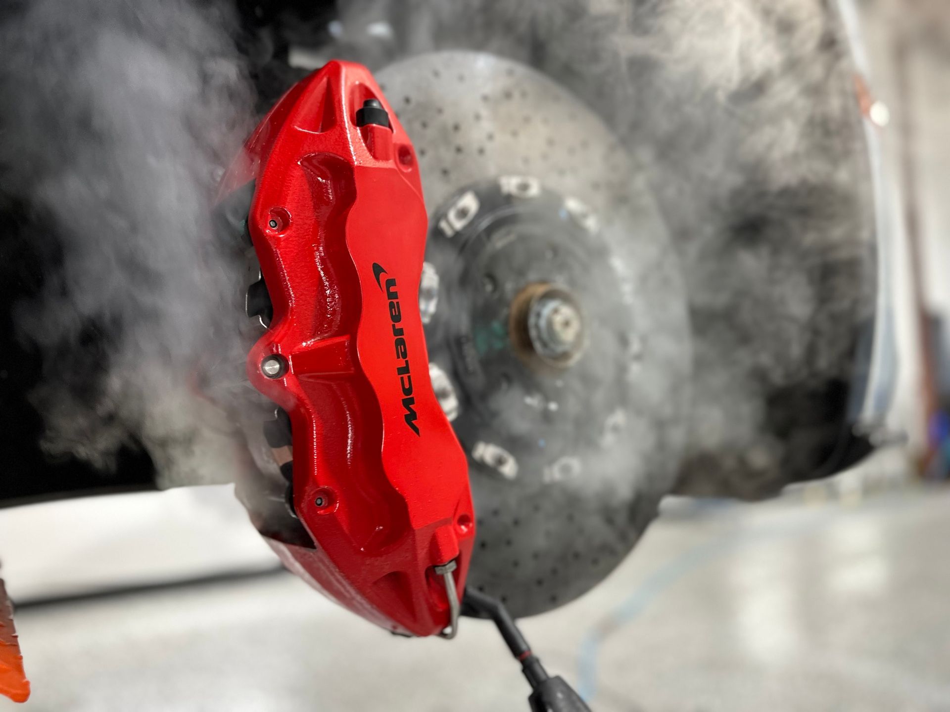 A red mclaren brake caliper with smoke coming out of it