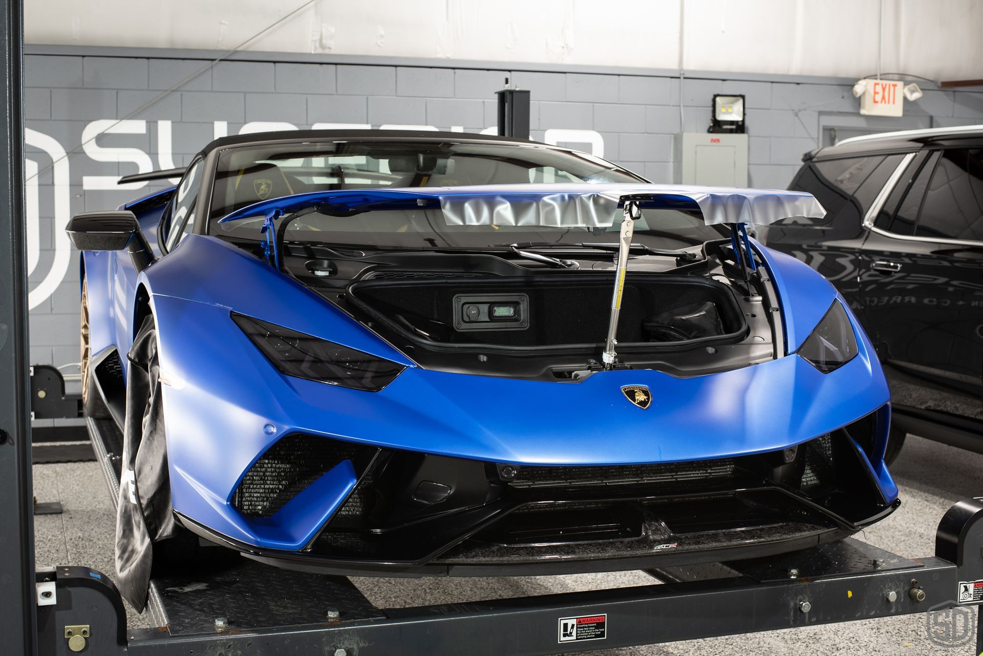 A blue lamborghini huracan is sitting on a lift with its hood open.