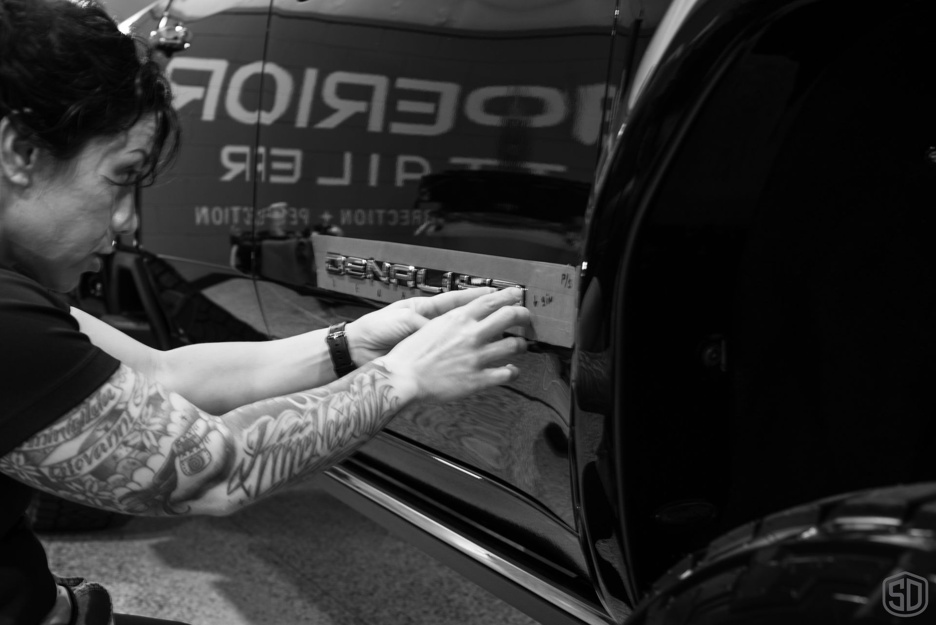 A black and white photo of a woman working on a car