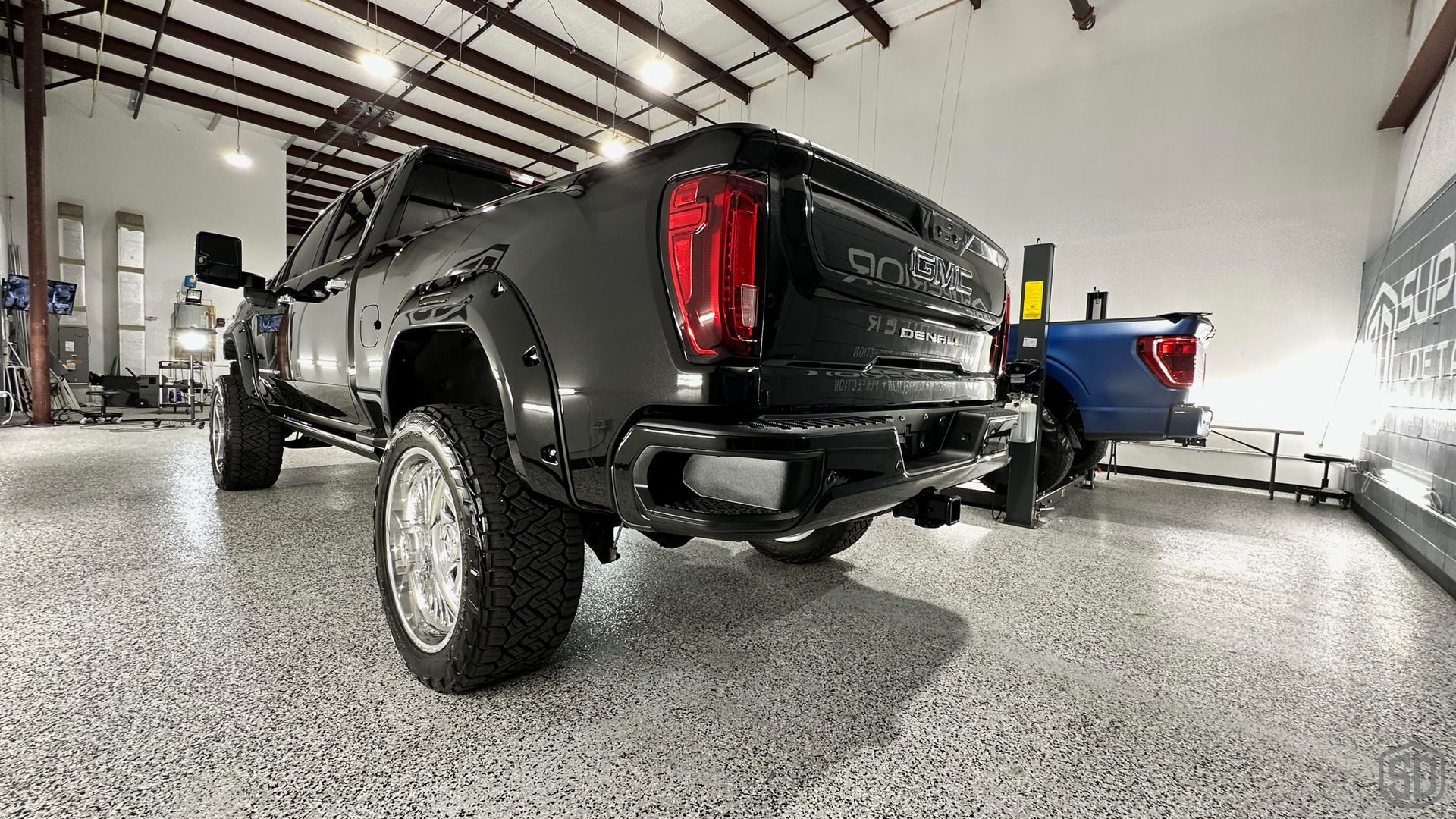 A black truck is parked in a garage next to a blue truck.