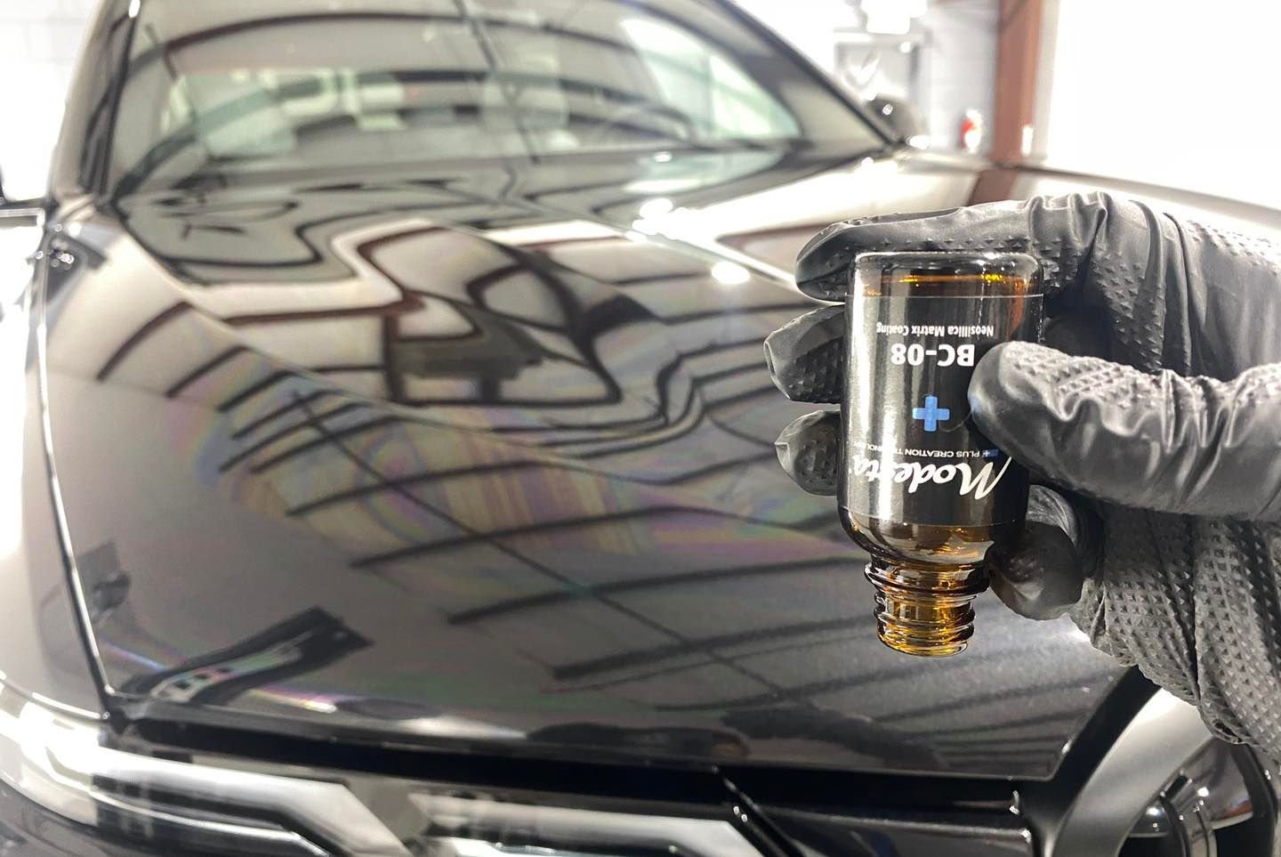 A person is holding a bottle of liquid in front of a car.