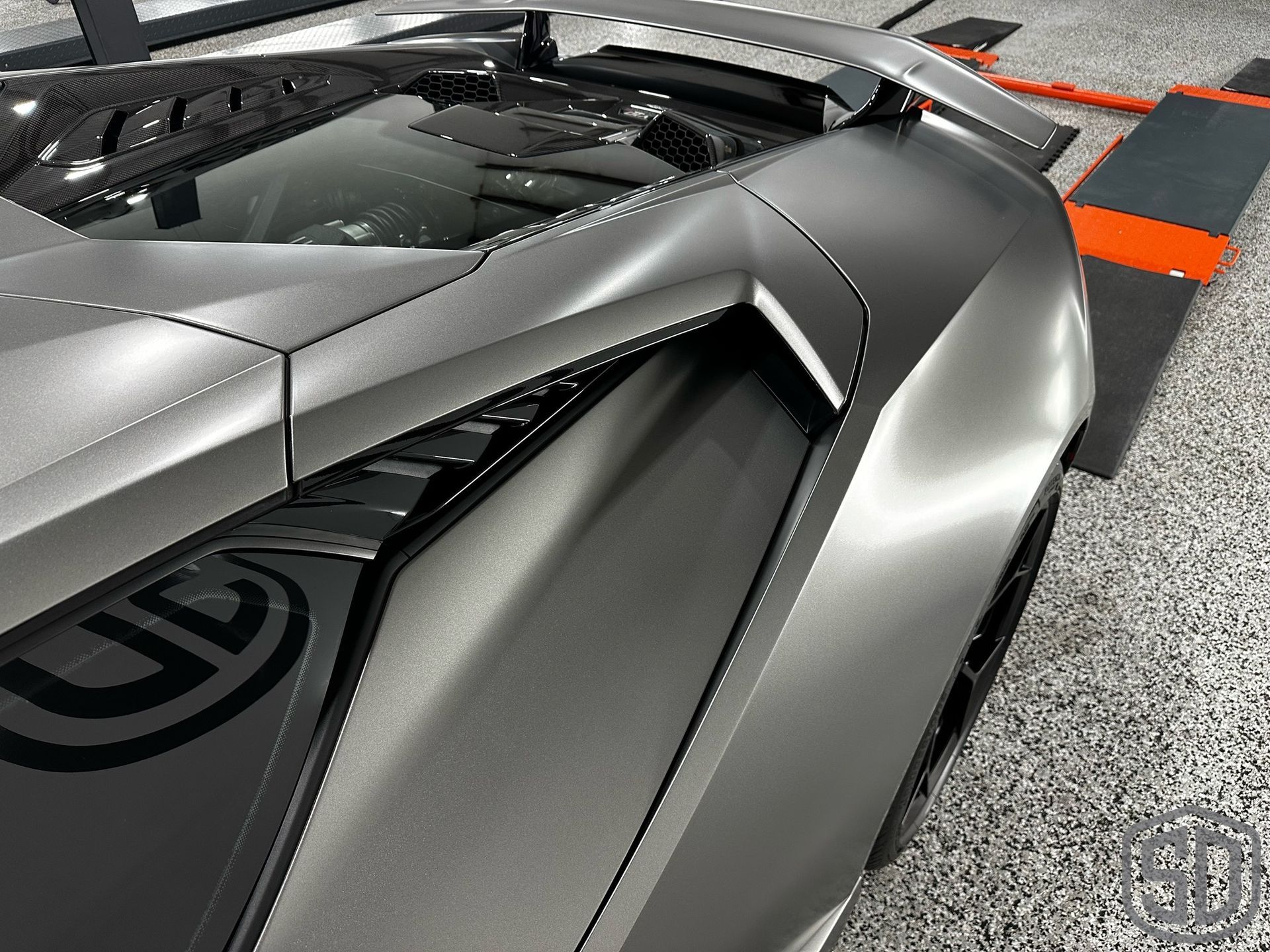 A gray sports car is parked in a garage with the hood open.