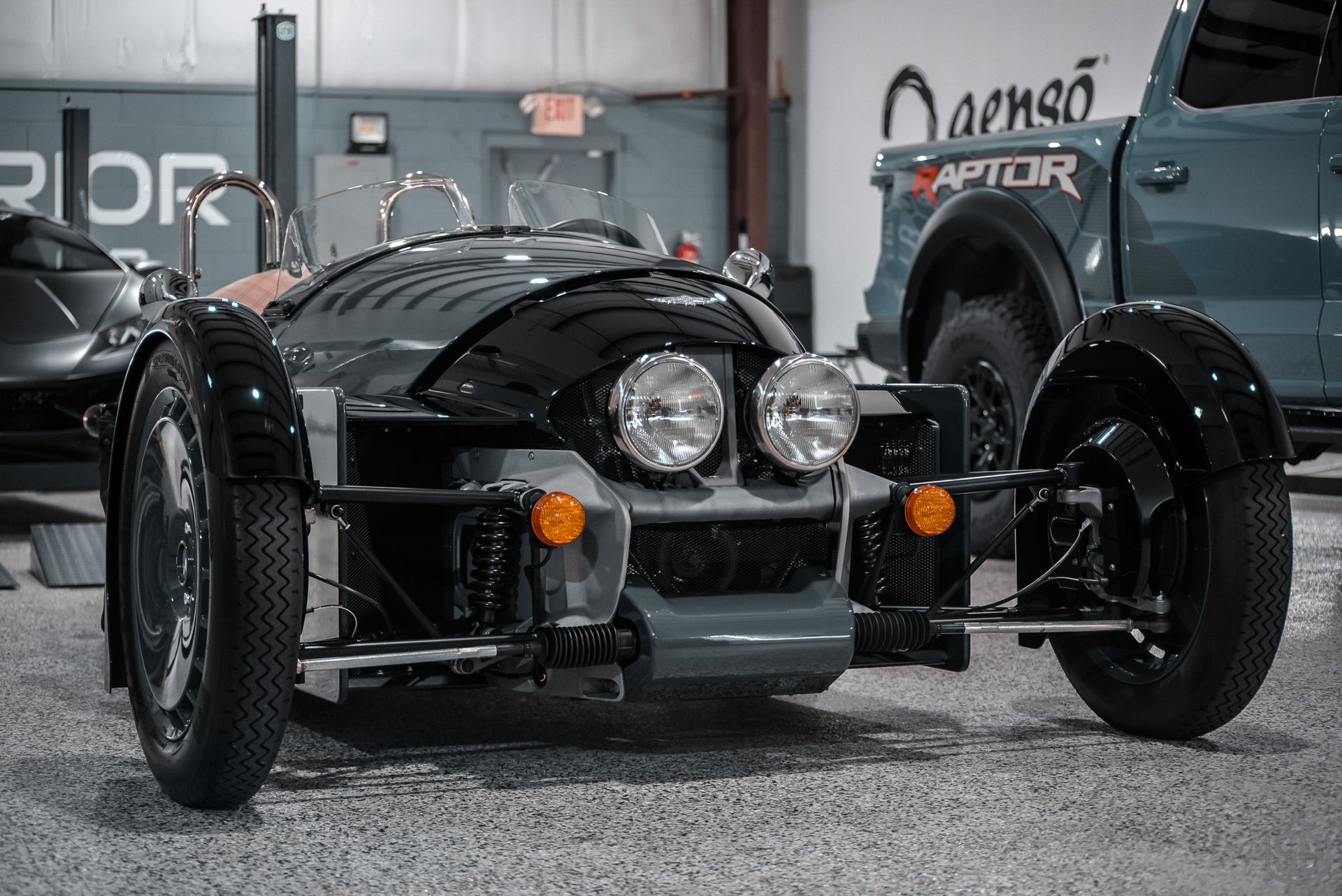 A three wheeled car is parked next to a truck in a garage.