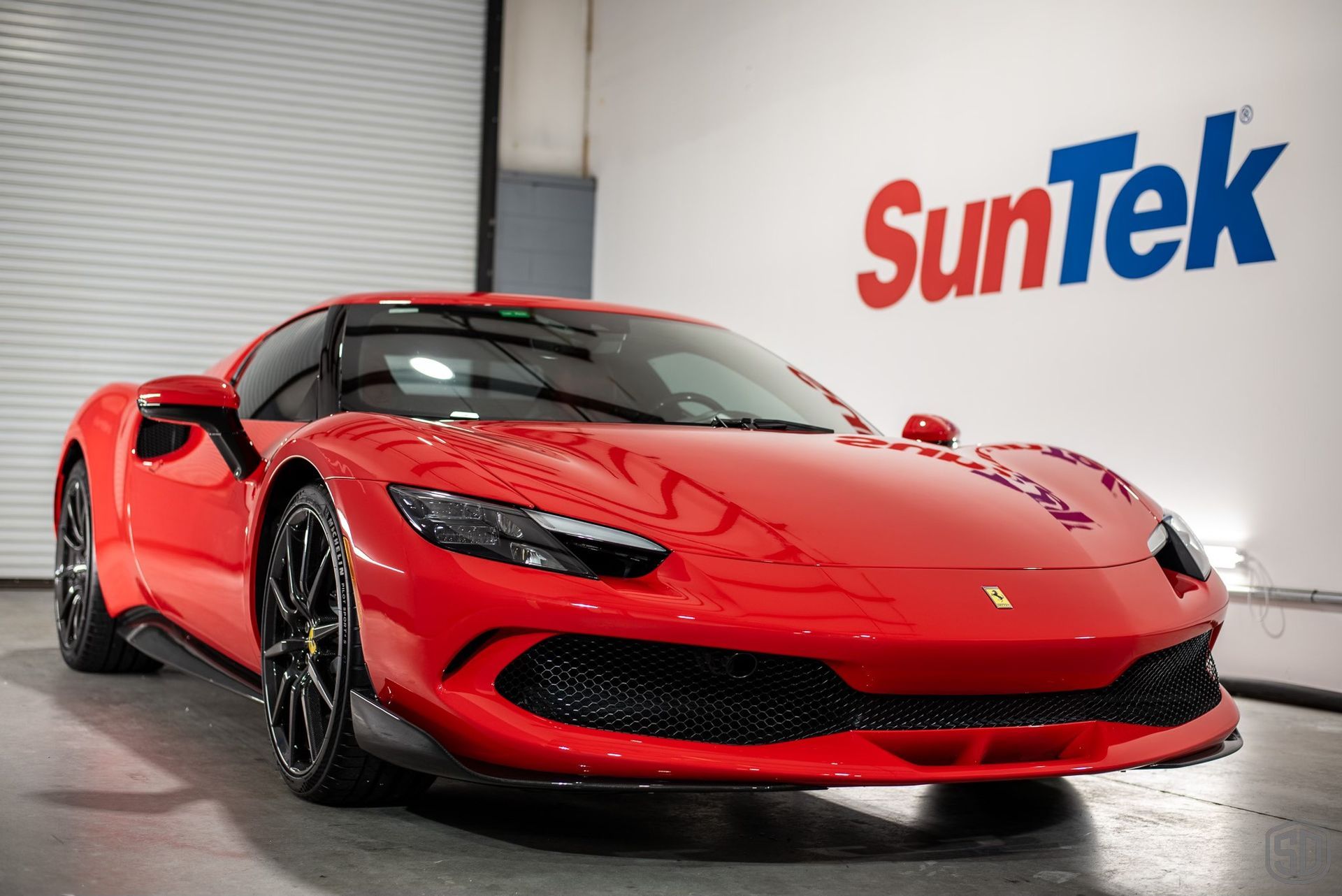 A red sports car is parked in front of a suntek sign.