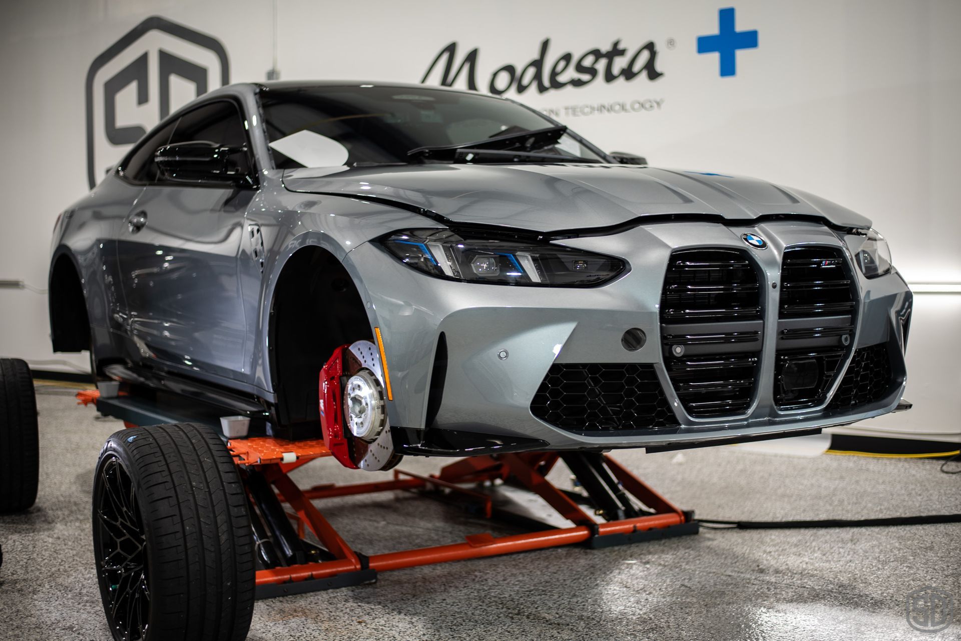 A bmw m4 is sitting on a lift in a garage.