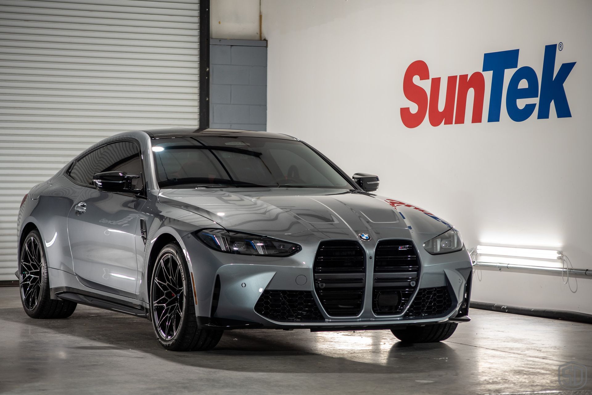 A bmw m4 is parked in a garage next to a suntek sign.