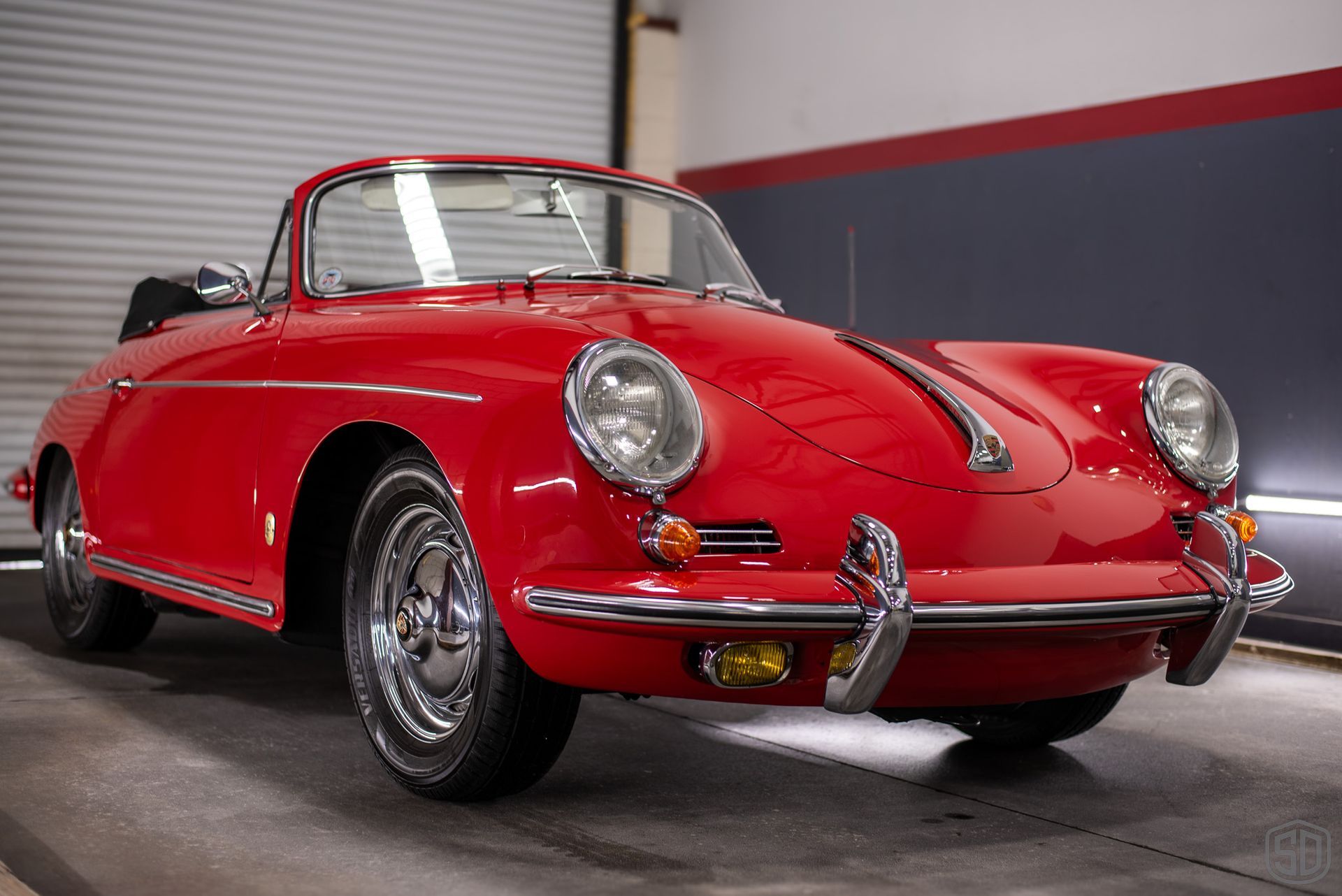 A red porsche is parked in a garage next to a garage door.