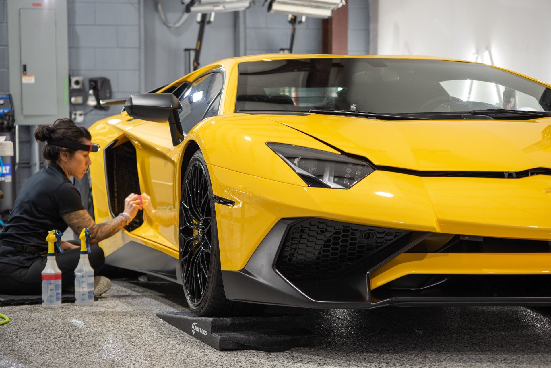 A woman is cleaning a yellow lamborghini aventador in a garage.