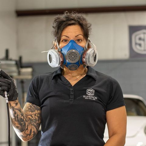 A woman wearing a mask and gloves is standing in front of a car