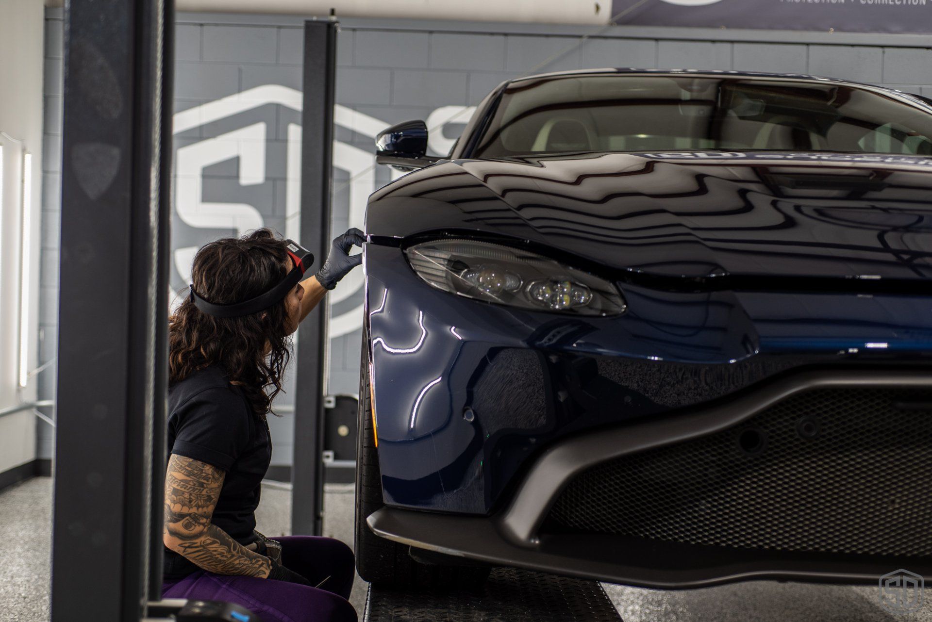 A woman is working on a car on a lift in a garage.