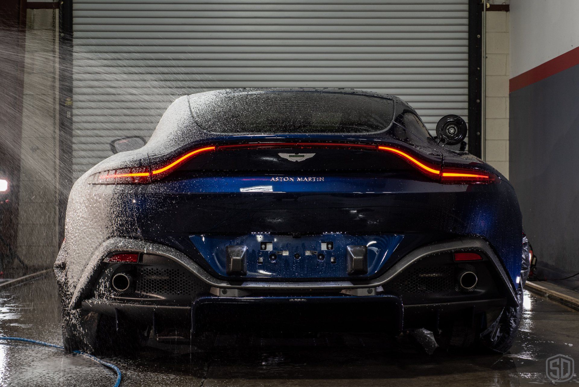 A blue sports car is being washed in a garage.