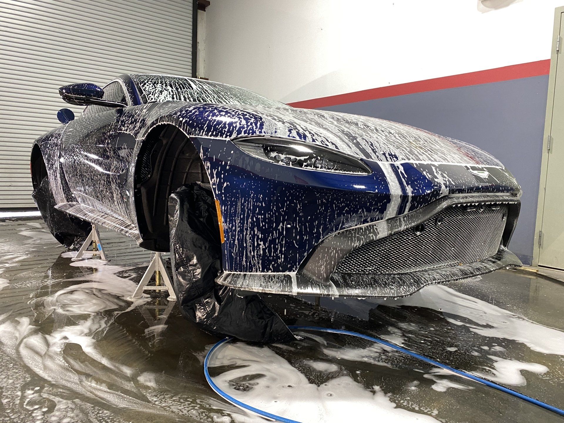 A blue sports car is covered in foam in a garage.