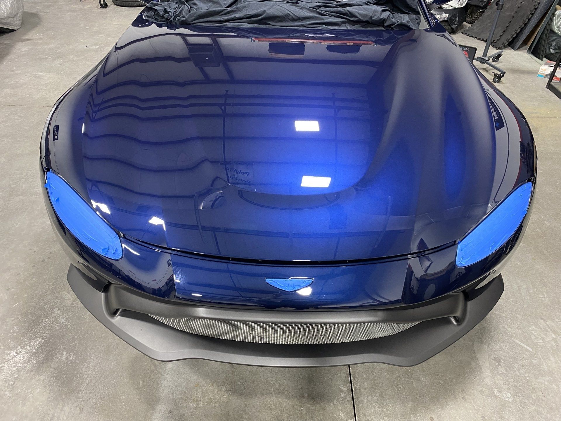 A blue car with the hood up is sitting in a garage.