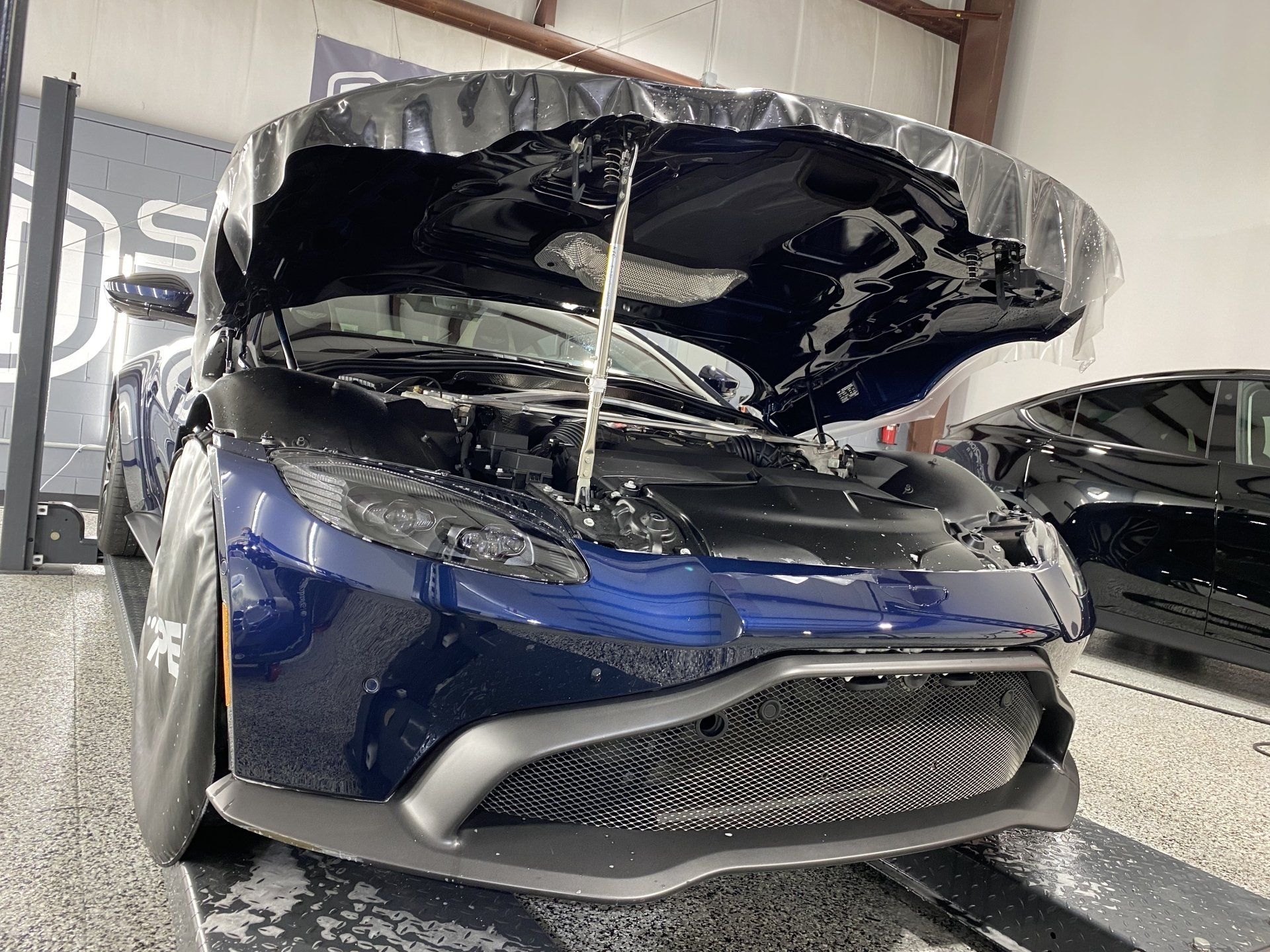A blue car with the hood up is sitting in a garage.
