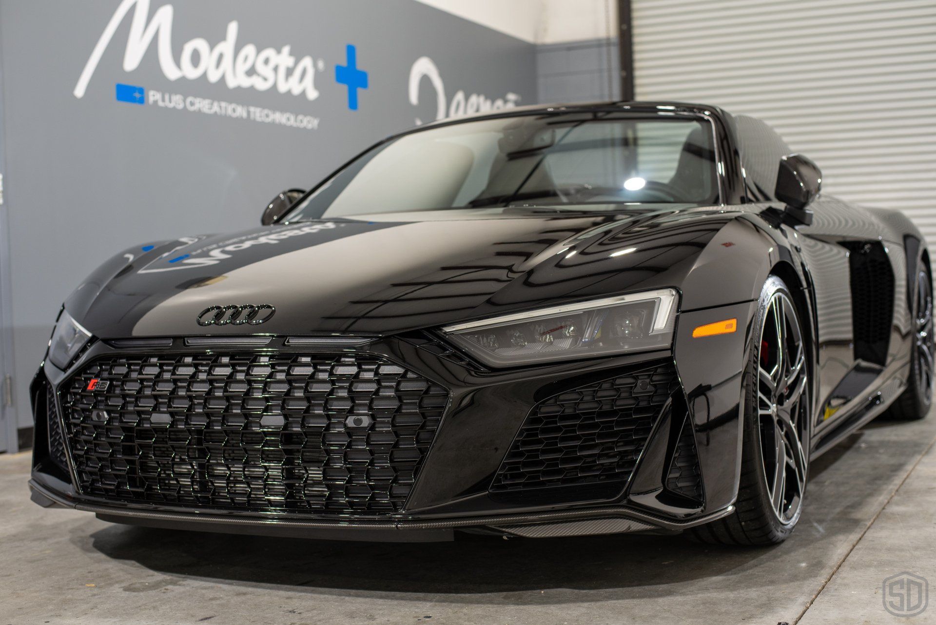 A black audi r8 is parked in front of a garage door.