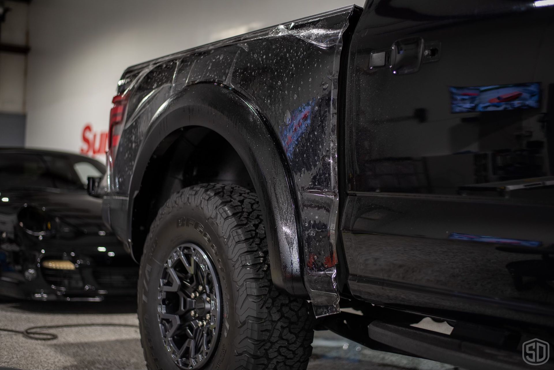 A black truck is parked in a garage next to a black car.