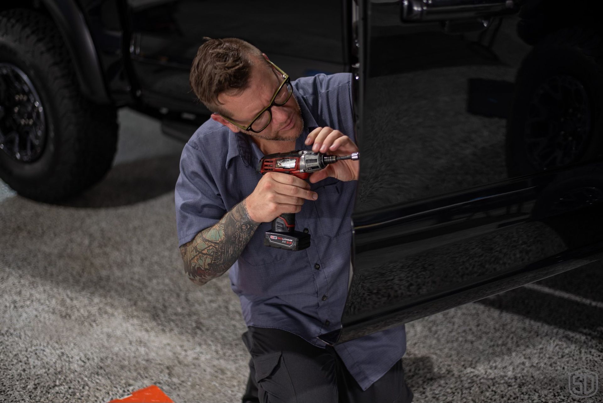 A man is kneeling down in front of a truck using a drill.