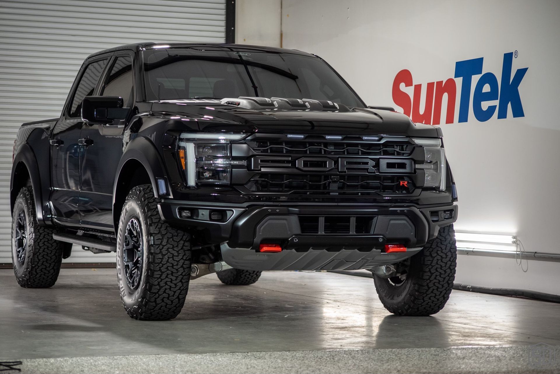 A black ford raptor is parked in front of a suntek sign.