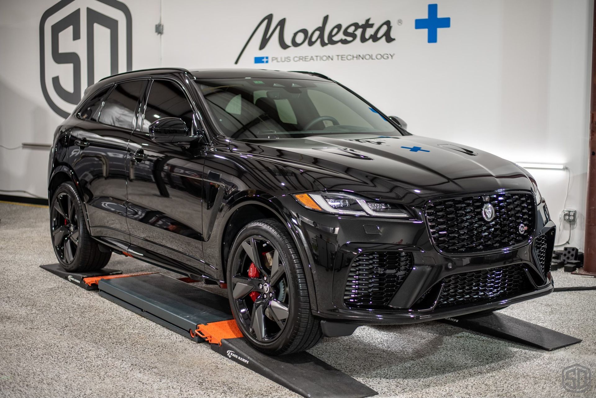 A black jaguar f pace is sitting on a lift in a garage.