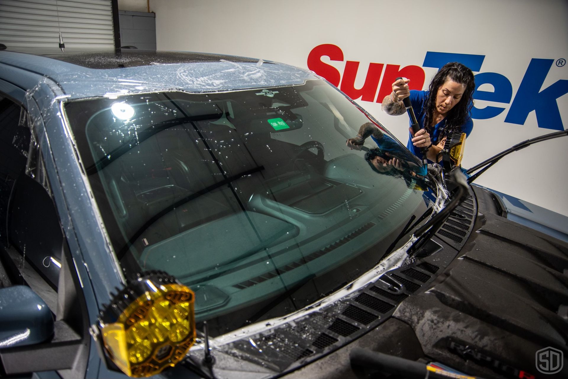 A woman is cleaning the windshield of a car.