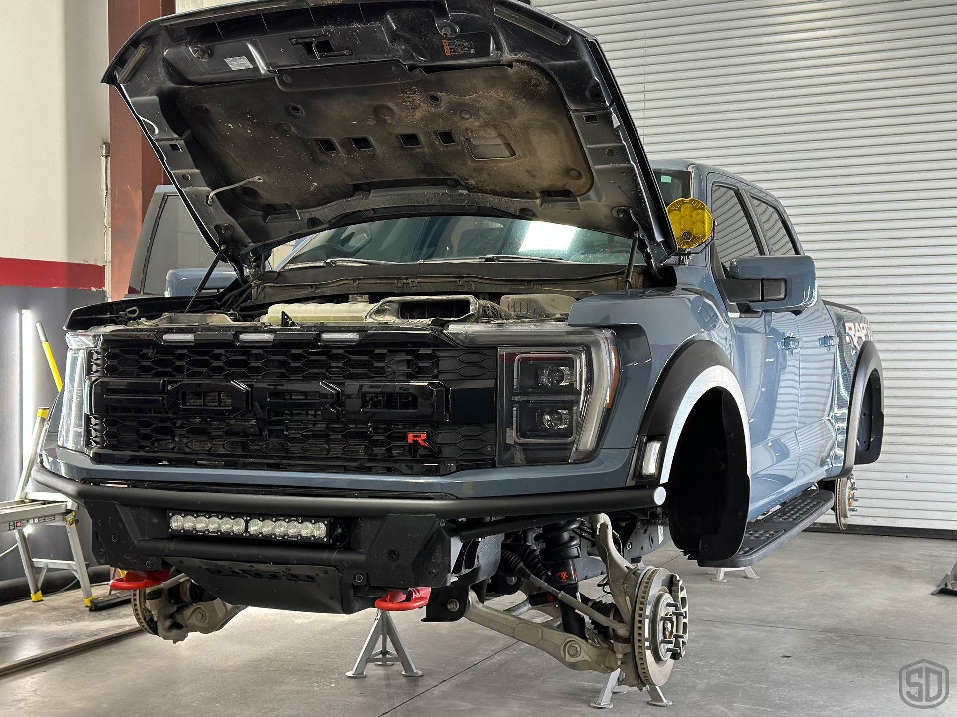 A ford f150 raptor is being worked on in a garage with the hood up.