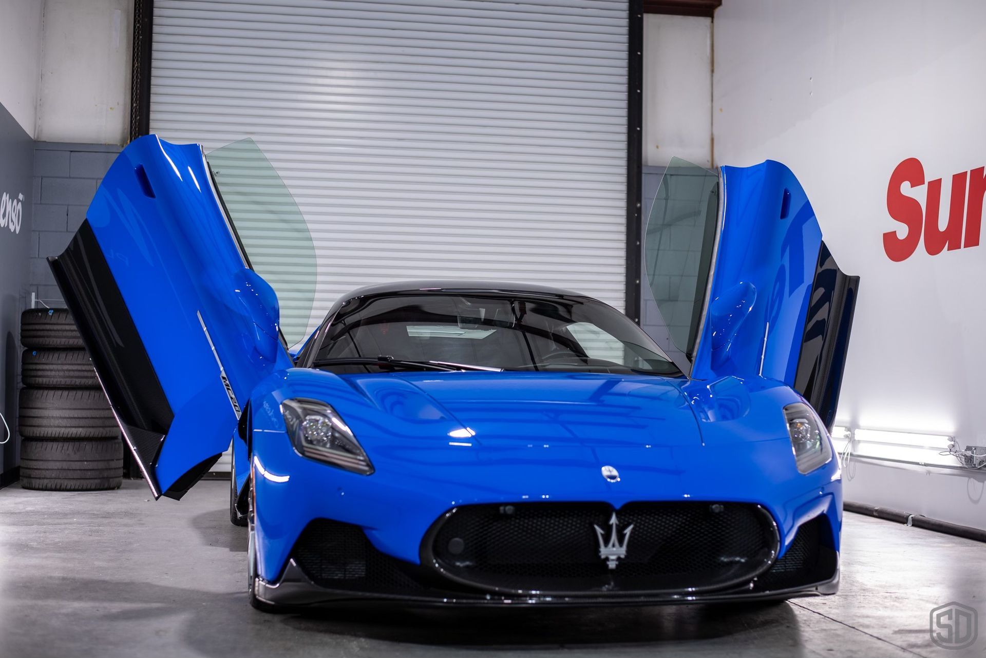 A blue sports car is parked in a garage with its doors open.