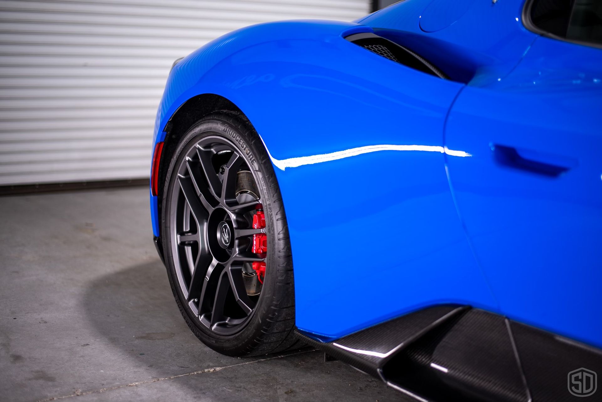 A blue sports car with red brake calipers is parked in a garage.