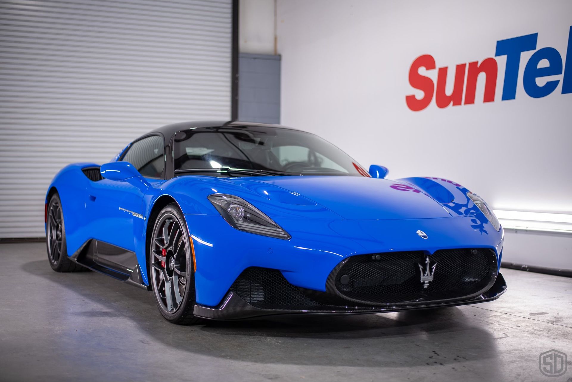 A blue sports car is parked in front of a suntech sign.