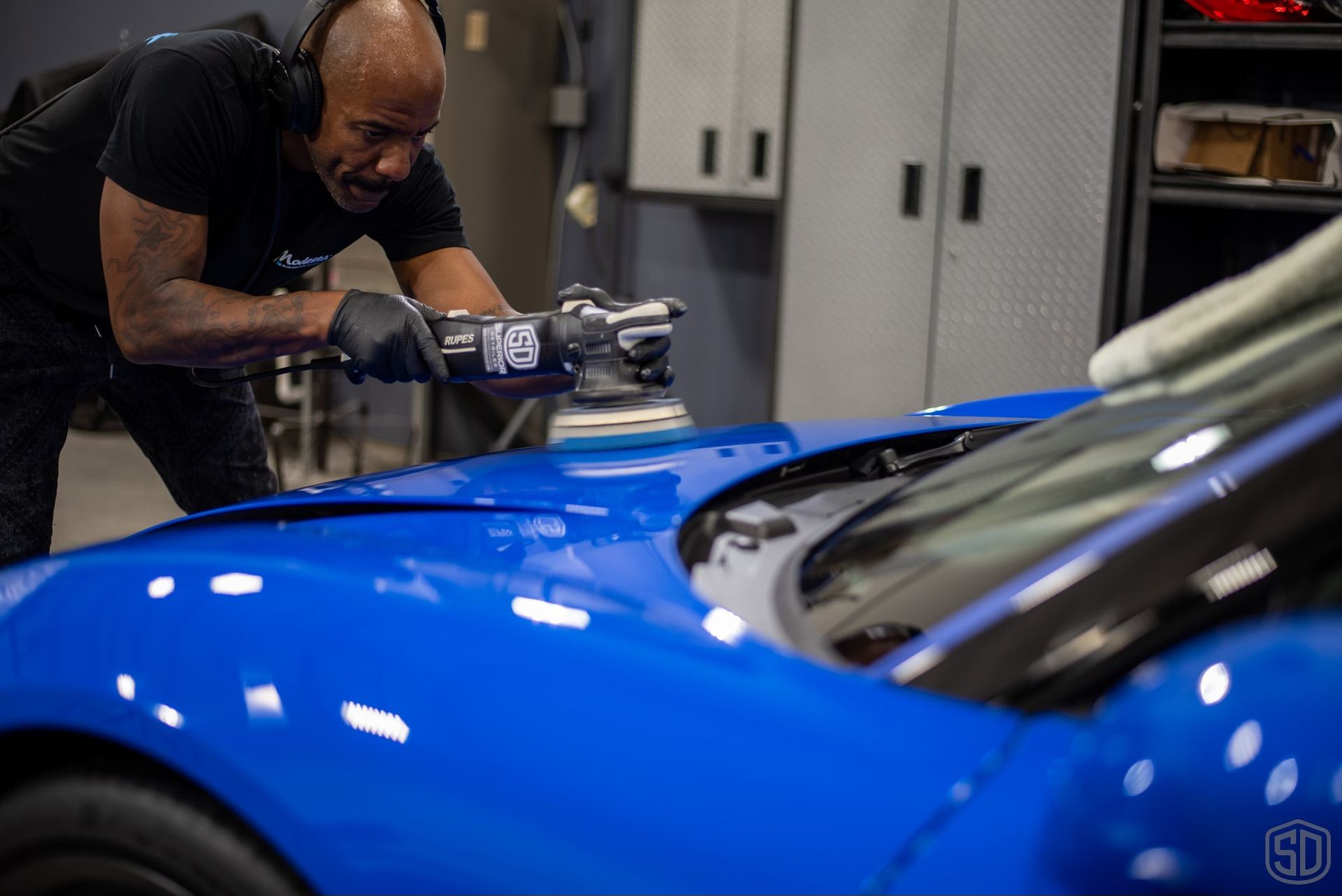 A man is polishing a blue car in a garage.