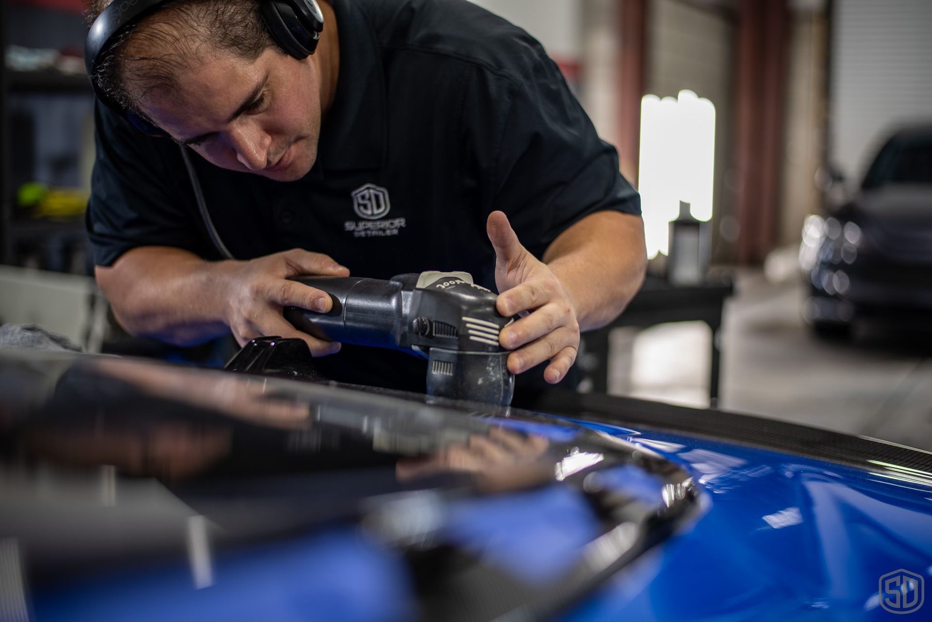 A man wearing headphones is polishing a blue car.
