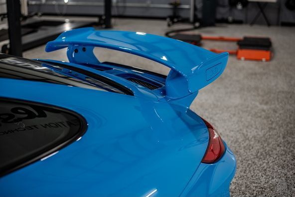 A blue car with a spoiler on the back is parked in a garage.