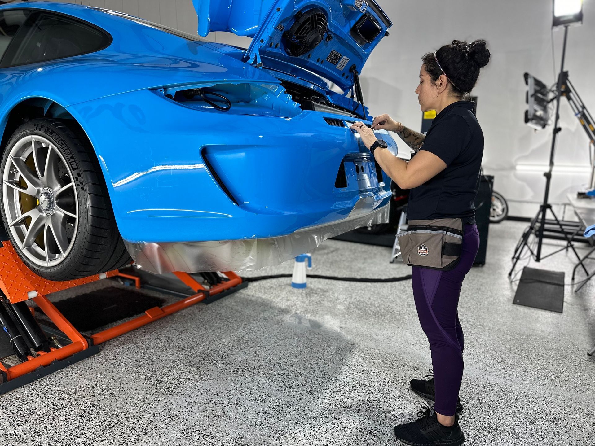 A woman is working on a blue sports car in a garage.