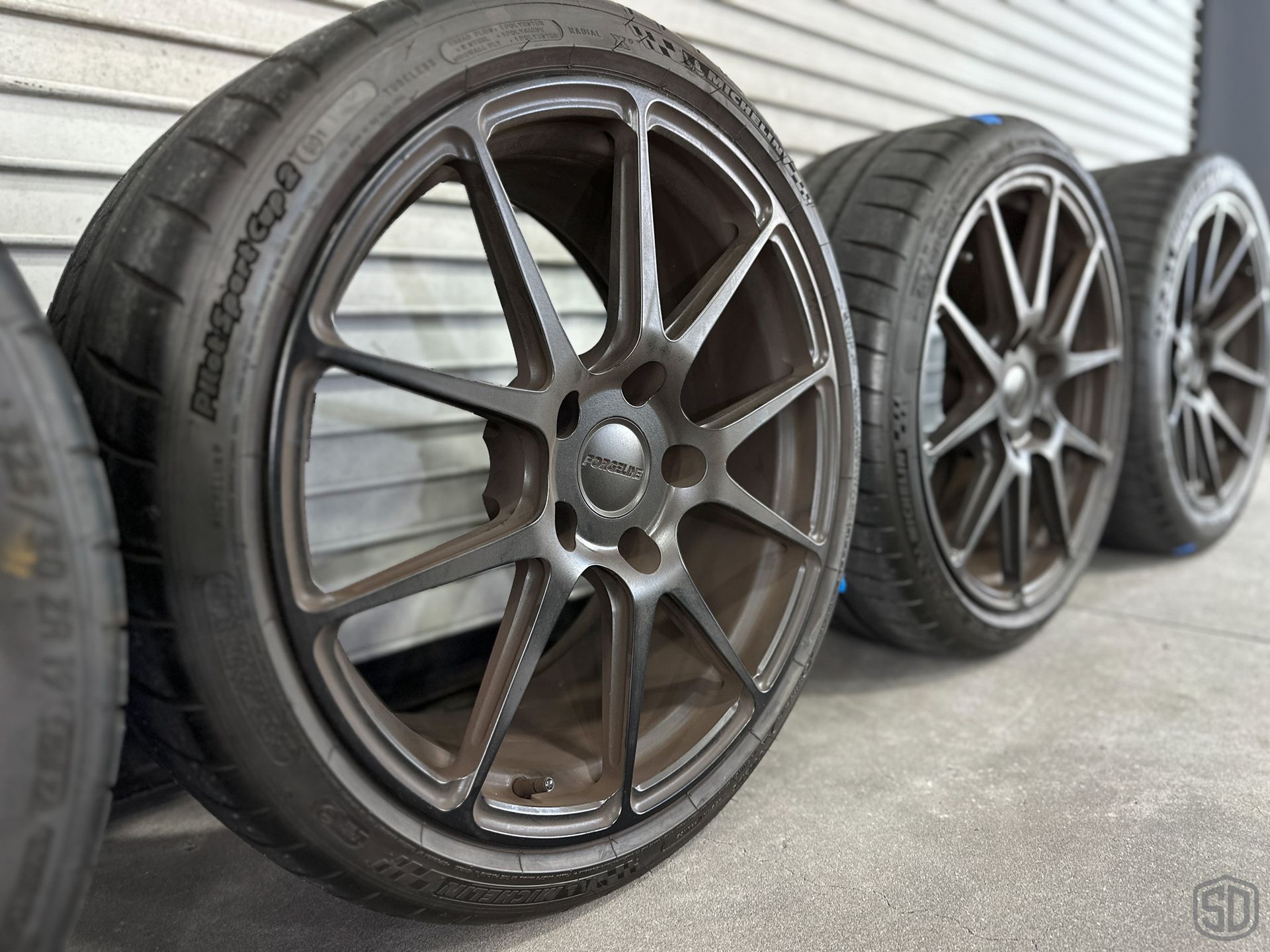 A row of tires and wheels are lined up against a wall; before pic
