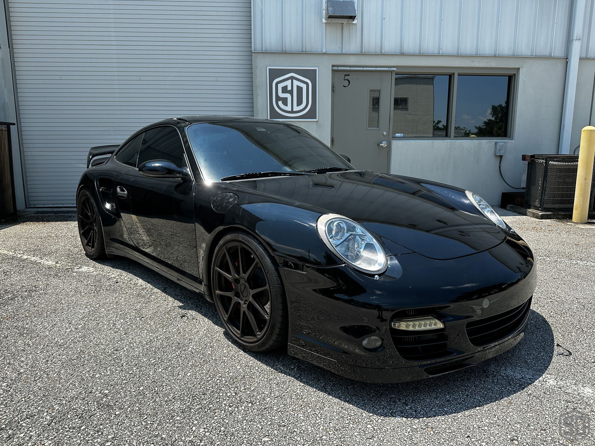 A black porsche 911 before detailing is parked in front of a building.