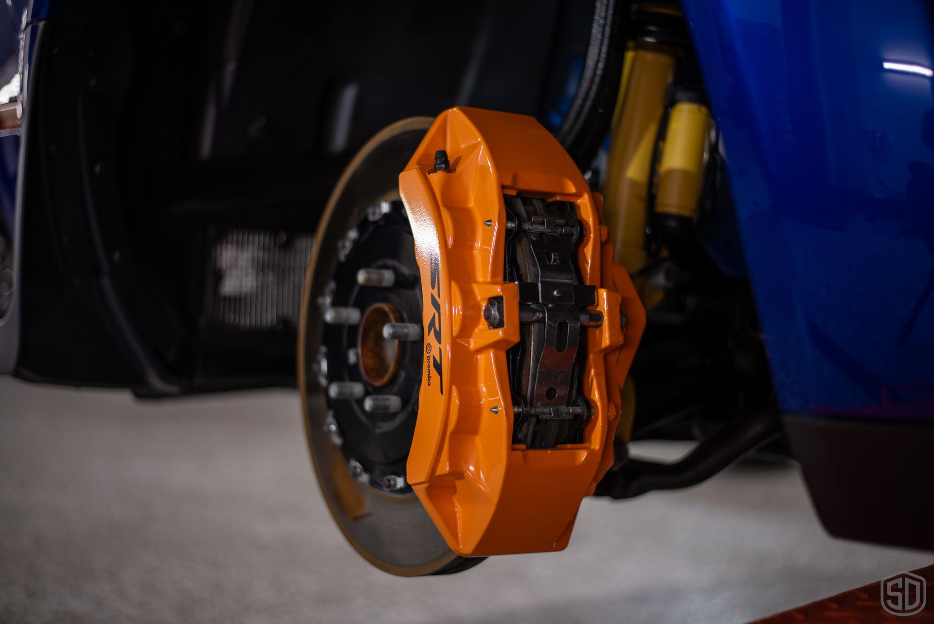 A close up of an orange brake caliper on a blue car.