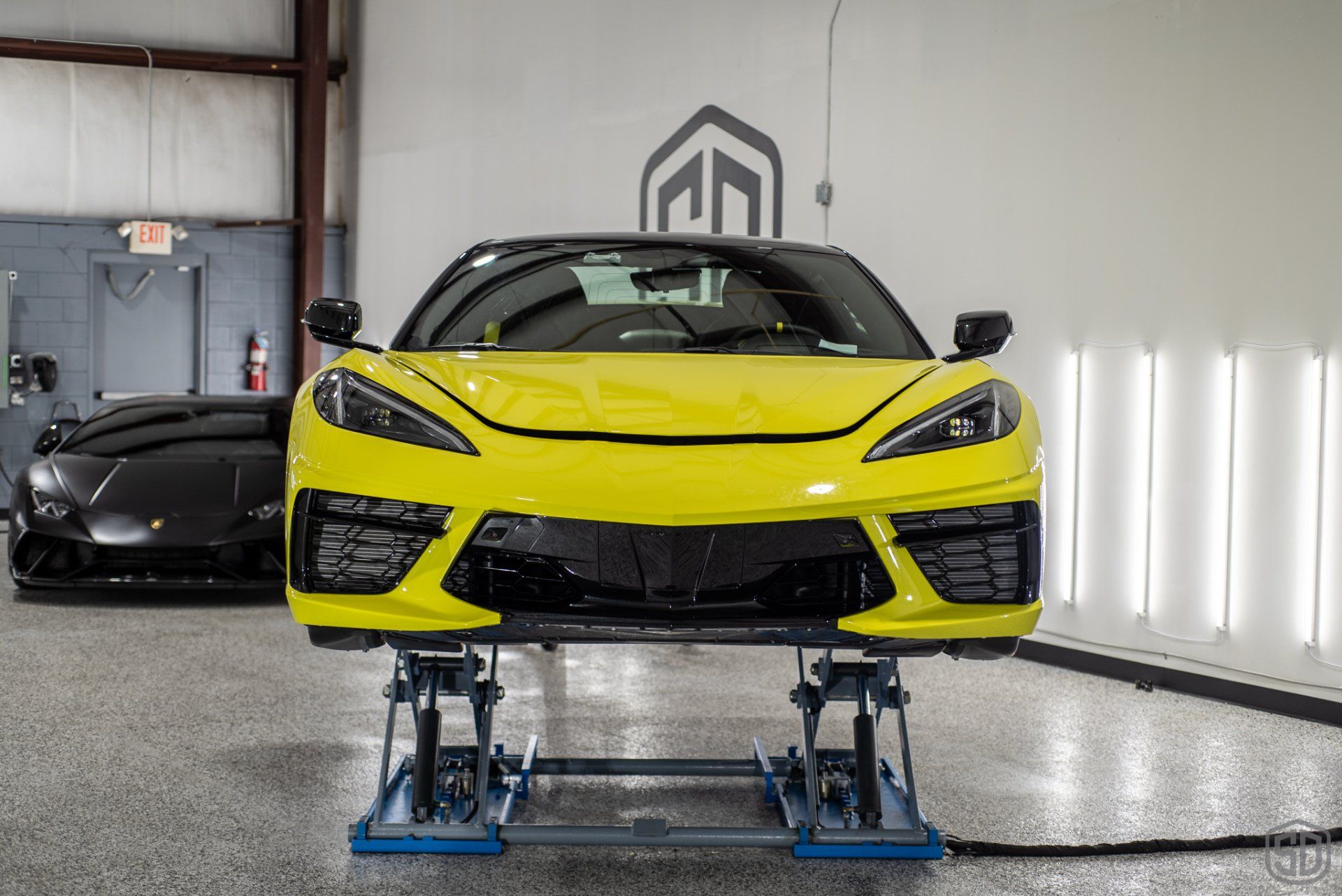 A yellow corvette is sitting on a lift in a garage.