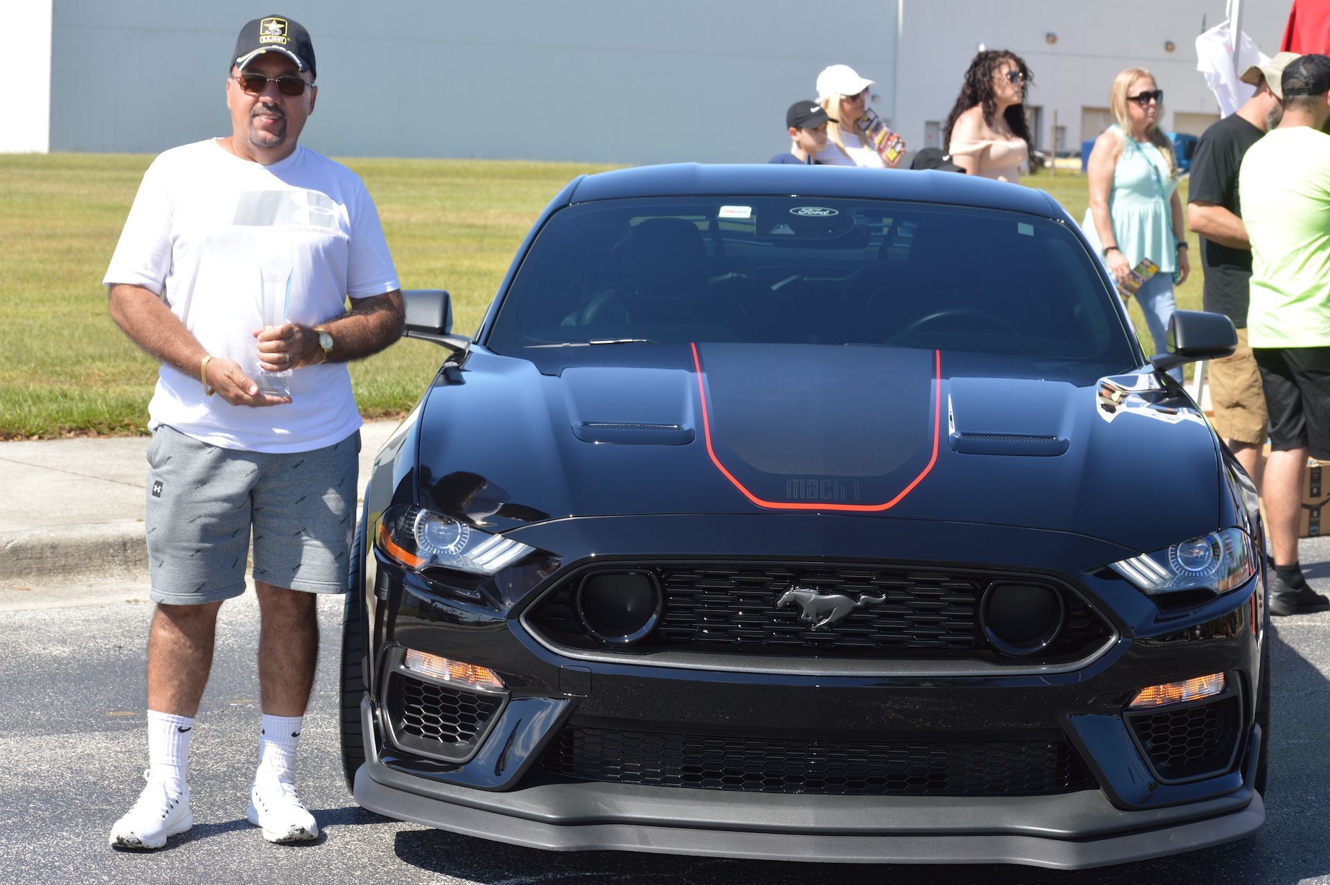 A man is standing next to a blue mustang with a red stripe on the hood.