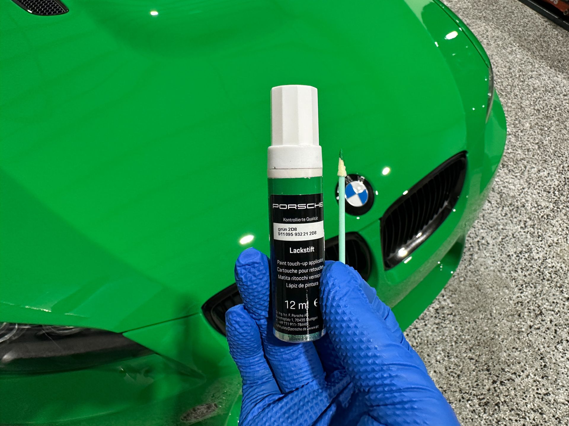 A person is holding a bottle of paint in front of a green bmw.
