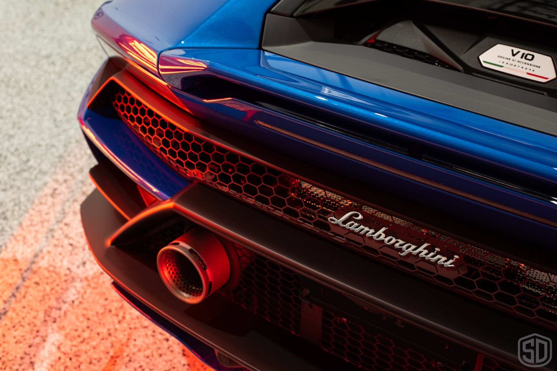 The rear end of a blue lamborghini with a red exhaust pipe.