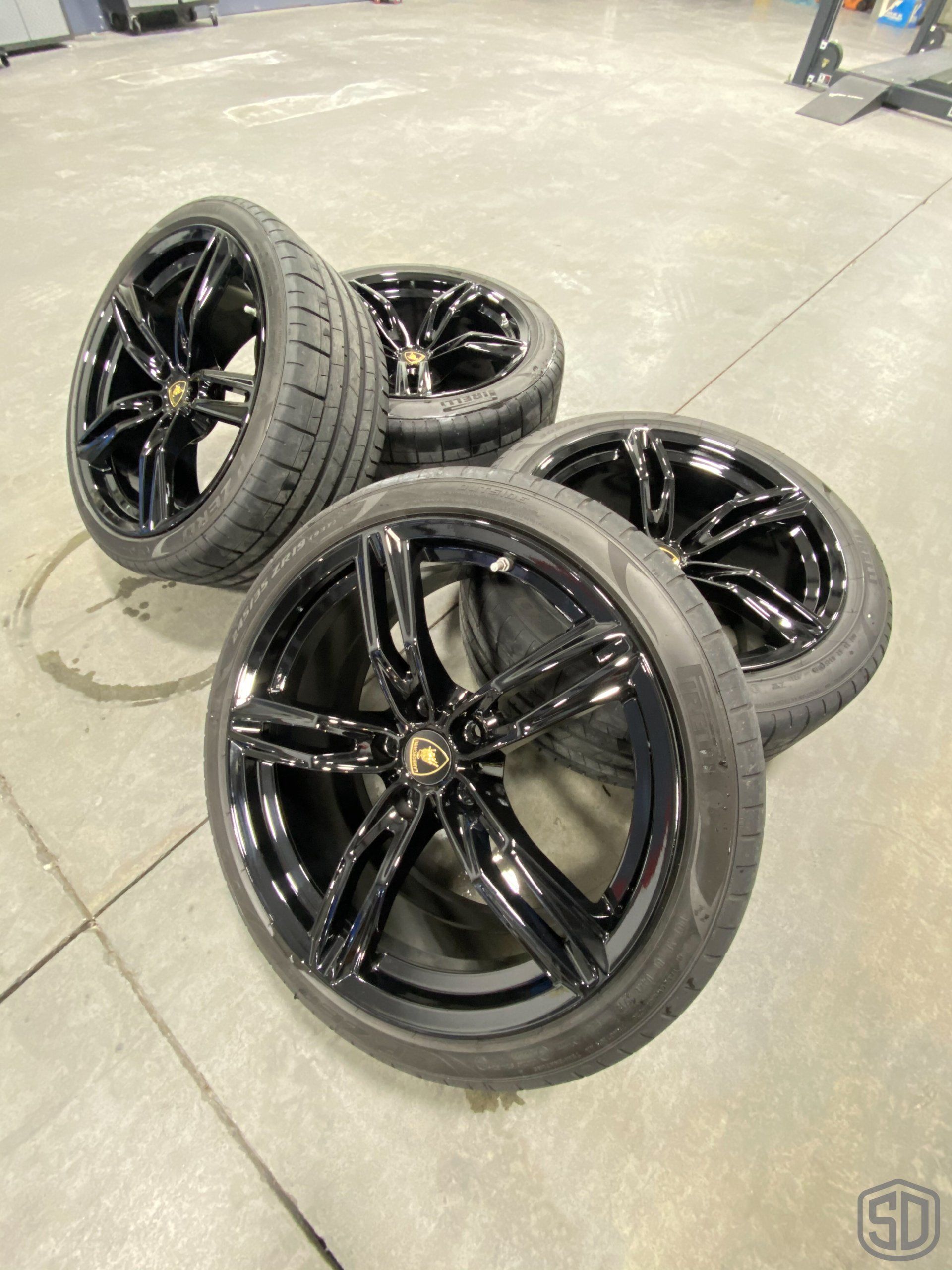 A set of black wheels and tires are sitting on a concrete floor.