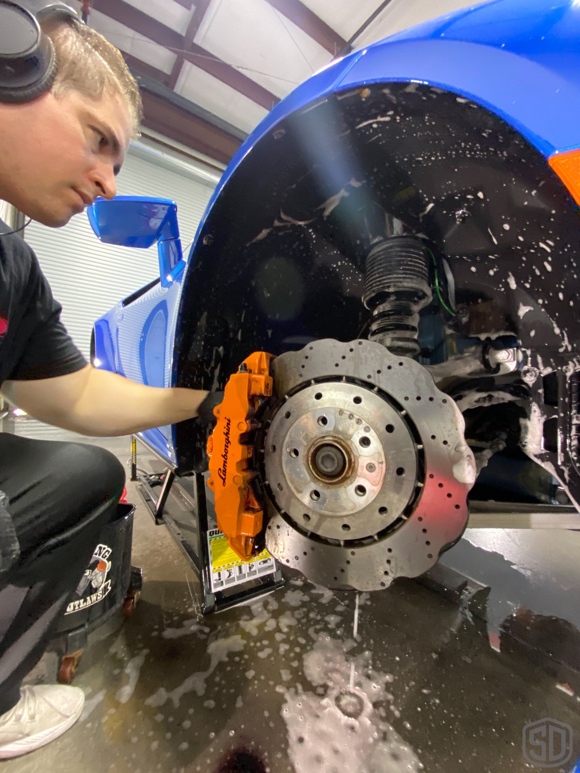 A man wearing headphones is working on a blue car