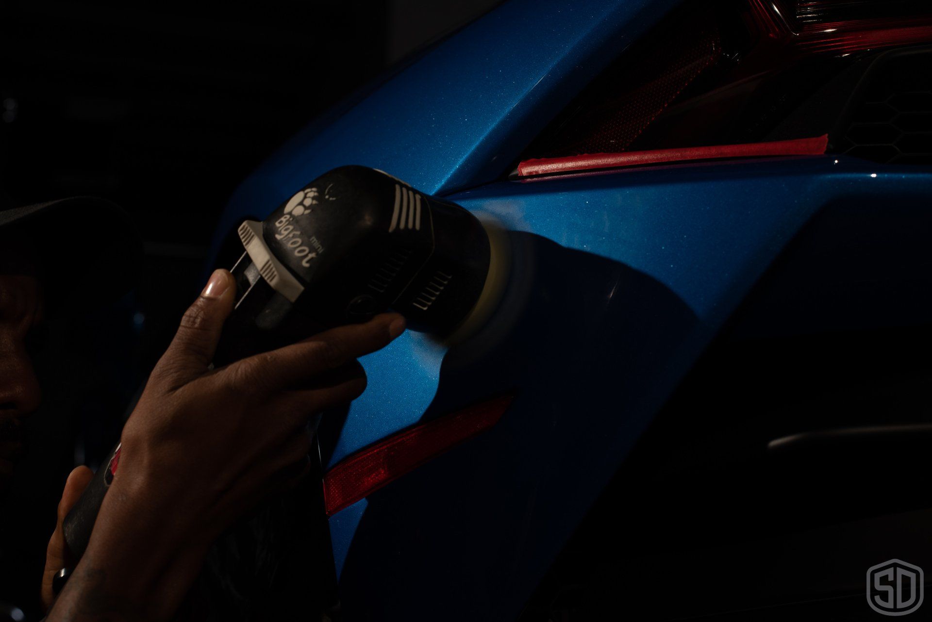 A person is polishing a blue car with a machine.