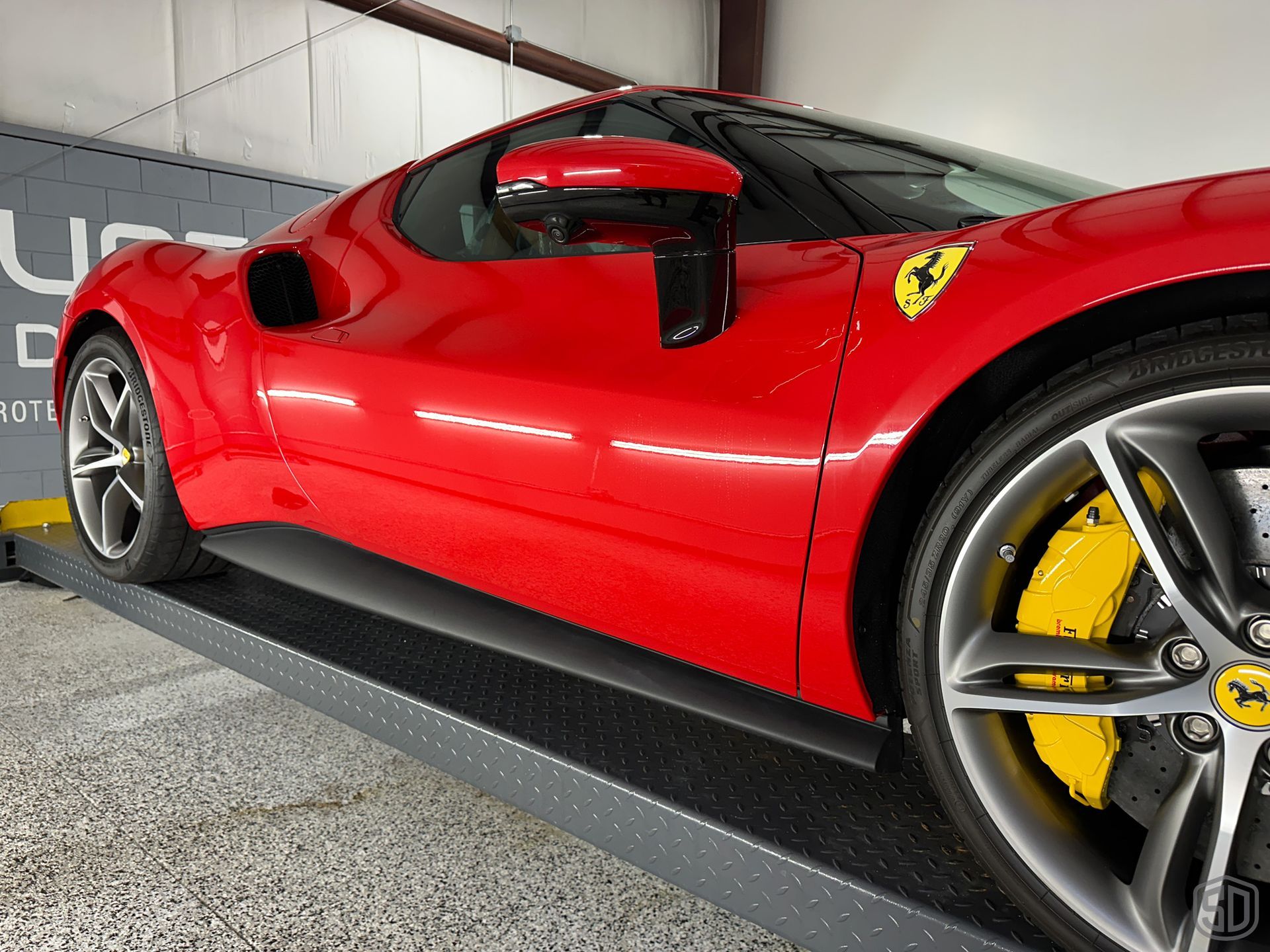 Red Ferrari sports car on a lift yellow brake calipers, black side mirror, and Ferrari logo visible.